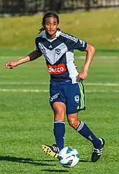 un footballeur en maillot bleu et blanc en train d'effectuer une passe du pied droit