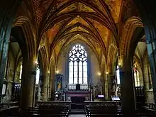 À droite et à gauche, des arcades reposant sur des piliers massifs. La voûte est richement décorée de peintures. Au centre, la grande baie du pignon. Derrière les piliers, les deux bas-côtés.