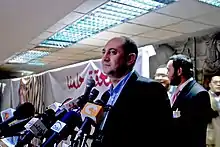 Khaled Ali de profil, regardant vers la gauche, devant des micros tendus vers lui.