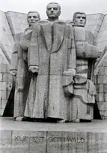 Photo noir et blanc montrant une sculpture en pierre de trois hommes debout, titrée « Klement Gottwald ».