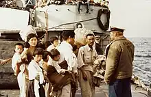 Photographie d'une groupe d'une dizaine de réfugiés, la plupart enfants, sur le pont d'un bateau américain.