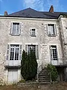 Photographie en couleurs d'un bâtiment dont la porte s'ouvre à l'entresol par un escalier en façade.