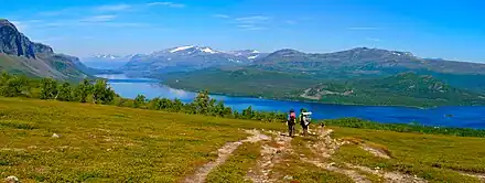 Deux randonneurs marchant vers un cours d'eau, au milieu d'un paysage montagneux.