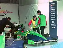 Photo du stand d'un pilote de course, où se trouvent une monoplace verte et des ingénieurs