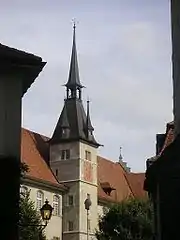 Photo en couleur d'un bâtiment avec toit rouge pentu, tourelle et clocheton, sur fond de ciel bleu.