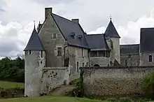 Photographie en couleurs d'un pont franchissant des douves, un muraille et des anciens bâtiments venant le cerner de part et d'autre.
