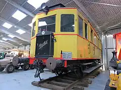 Photographie en couleurs montrant une vue de trois quart avant de l’autorail, livrée jaune avec liserés rouges.