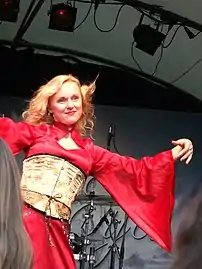 Une femme blonde portant une robe rouge et jaune se produit sur scène