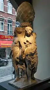 Sculpture détériorée montrant trois femmes adossées à une colonne surmontée d'une grosse pomme de pin