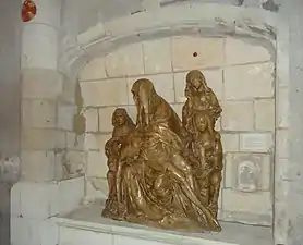 Vue de côté d'un groupe sculpté en bois placé dans une niche d'un mur en pierre.