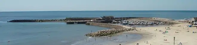 Vue panoramique. La pleine mer et un port bien protégé par sa jetée.