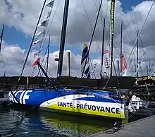 Vu de trois quarts arrière, voilier bleu, blanc et jaune amarré au ponton.