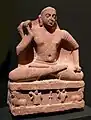 Le Buddha kapardin en dhoti sur le trône aux lions. empire kouchan, fin Ier&nbsp;siècle ou début IIe&nbsp;siècle. Région de Mathura. Grès rose tacheté. Linden-Museum, Stuttgart