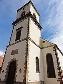 Photographie couleur d'un clocher surmontant une façade d'église.