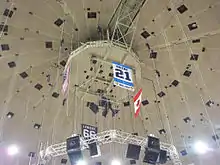 Photo de la bannière dédiée à Michel Briere au milieu de câbles tombant du plafond de la Mellon Arena; on distingue également les drapeaux américains, canadiens et la bannière dédiée à Mario Lemieux.
