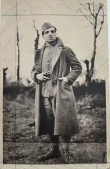 Photographie en noir et blanc d'un homme moustachu debout, vêtu d'un uniforme militaire.