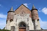 Deux échauguettes en brique supportées par des contreforts en pierre calcaire et percées de meurtrières protègent l'entrée de l'église.