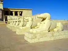 Décor de cinéma défraîchi, représentant un palais égyptien et une rangée de sphinx à têtes de crocodiles.