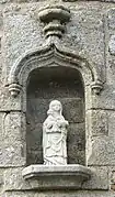 Photographie d'une niche de façade en granit, contenant une statuette.