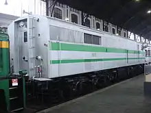 Photo couleur montrant l'arrière d'une loco blanche à bande verte. Une porte permet la circulation avec le train, mais il n'y a pas de vitre de cabine.