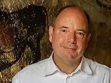 Photographie en couleurs et en buste d'un homme en vêtu d'une chemise blanche.