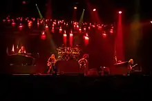 Cinq membres d'un groupe de rock jouant devant un écran projetant des bougies