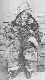 Photographie en noir et blanc d'un homme assis portant un habit en fourrure.