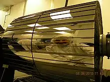 Photo d'une optique, comme un cylindre d'une couleur doré sombre avec le reflet d'un technicien dedans.