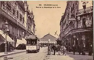 Rue avec deux rangées de bâtiments avec la gare au fond.