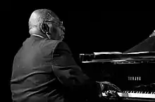 Photographie en noir et blanc d'un homme de dos qui joue du piano.