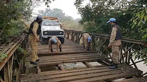 Photographie de soldats aux casques bleus en cours de réparation d'un pont pour y faire passer un véhicule.