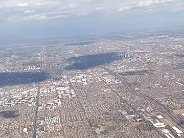 Photographie aérienne cadrée sur une agglomération entourée de zones montagneuses, où les zones urbaines sont clairement différenciées.
