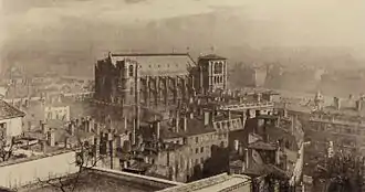 Photographie sépia d’une cathédrale dominant un quartier urbanisé, le tout dans la brume.