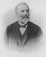 Photographie en noir et blanc d'un homme d'âge mûr avec une barbe blanche et un costume sombre.