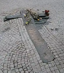 Une croix stylisée au sol, entourée par les pavés du sol, avec des roses.