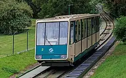 Un funiculaire vert et beige descend une colline verdoyante.