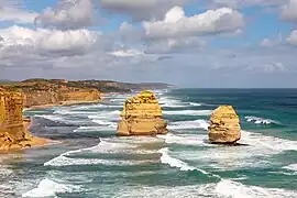 Sur une côte de falaises parcourue de vagues écumeuses, deux hauts îlots en forme de cheminées se dressent dans la mer.