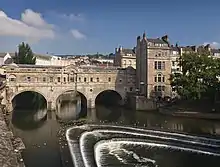 Un pont à trois arches en pierre avec des bâtiments construits au-dessus. Au-dessous du pont se trouve le déversoir à trois étages.
