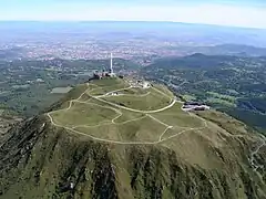 Vue aérienne du puy de Dôme depuis l'ouest avec Clermont-Ferrand au second plan et, à l'horizon, le mont Blanc, distant de 315&nbsp;km.