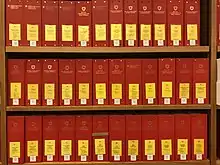 Photographie de 36 classeurs rouges avec étiquette jaune sur une étagère