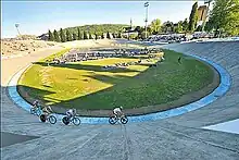 Photographie d'un vélodrome en plein air avec quatre coureurs en piste.