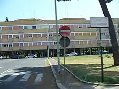 Une longue barre d'immeubles à la façade décrépie. La rue porte le nom de l'olympiade.