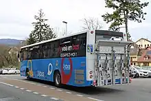 Photographie en couleurs d’un autocar bleu, blanc et noir vu de derrière, avec un porte-vélos à l’arrière.