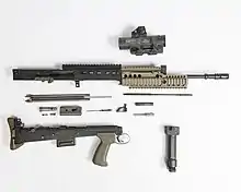 photographie en couleur montrant un fusil d’assaut démonté sur fond blanc à la manière d’un plan éclaté