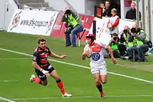 Joueur débordant sur le côté gauche du terrain, malgré l'arrivée d'un adversaire depuis son coté droit.