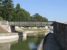  Photo couleurs. Passerelle franchissant le canal sur le bief de Saint-Jean-de-Braye. Il s’agit d’un pont en poutre droite en treillis, peint en gris.