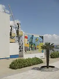 Photographie d'une place avec des installations portuaires à l'arrière-plan.