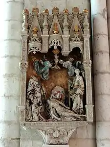 Sculpture représentant, dans un baldaquin sculpté et en partie doré, six personnages surmontés par deux petits anges. Parmi ces personnages, deux sont debout tandis que le troisième est au sol, soutenu par le quatrième personnage, une femme portant une robe bleue et rouge. Les deux derniers personnages, plus petits, sont agenouillés et prient. La sculpture est dans un état dégradé.