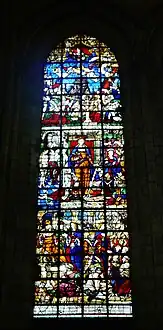 Grand vitrail représentant une vingtaine de personnages. Au centre de l'image, une femme habillée en orange porte une épée et un livre rouge. Des hommes sont agenouillés à ses pieds.