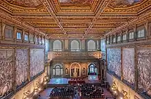 Photo de l'intérieur d'une immense salle. Les murs de droite et de gauche portent d'immenses fresques. Le mur de face porte une fontaine et des baies vitrées.